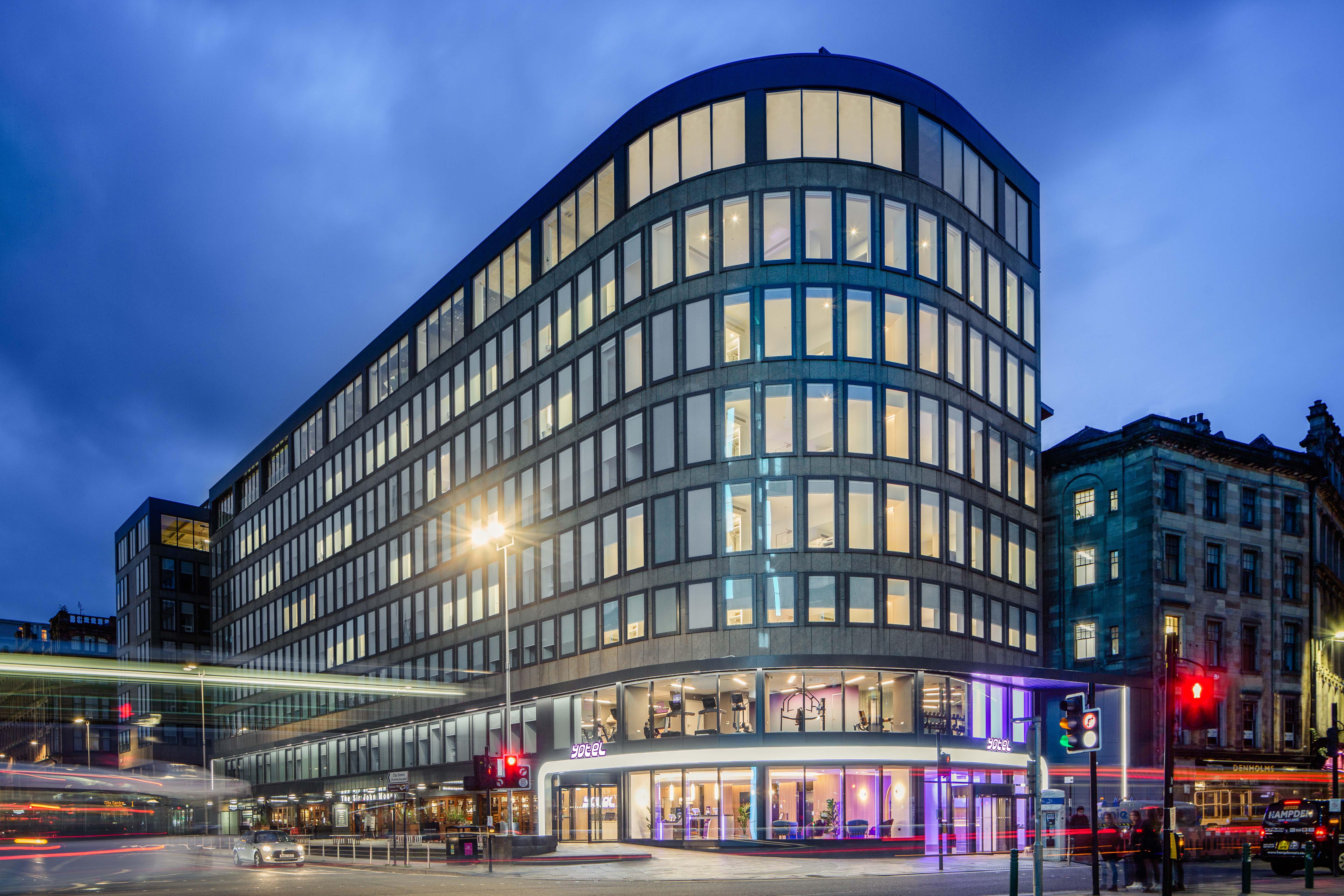 Yotel Glasgow Exterior foto The photo shows a modern office building with a distinctive curved shape and a facade made of large glass windows. It is illuminated against a twilight sky, giving it a contemporary appearance. The ground floor features large glass entrance areas, li